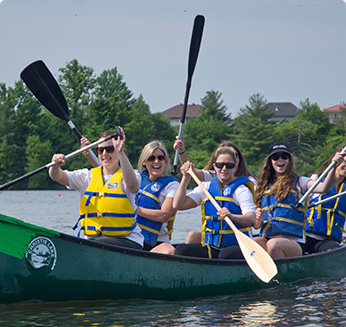 Photograph of group of people in a canoe on the lake, smiling and enjoying themselves.